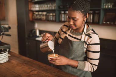 Trendy Cafe dökme frothed sütünü tezgahın arkasındaki genç Afrika barista ayakta içine bir fincan kapuçino gülümseyen 