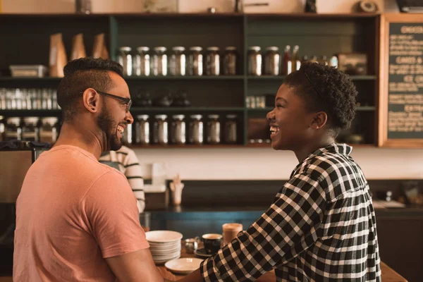 Smiling young couple talking and laughing together while standing at a counter in a cafe ordering drinks