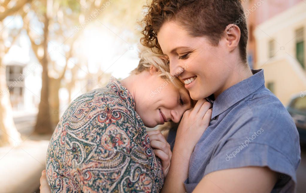 Content young lesbian couple hugging each other while standing together on a city street on a sunny day