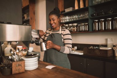 Bir kapuçino trendy kafesinde tezgahın arkasındaki için süt renginde solma genç Afrika barista gülümseyen