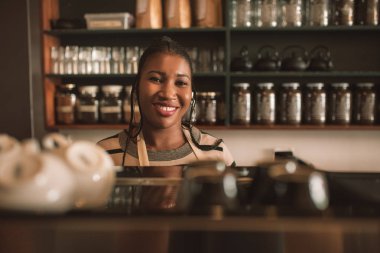 Welcomingly modaya uygun bir kafede sipariş tezgahın arkasındaki dururken gülümseyen genç Afrika barista portresi 