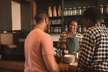 Gülümseyen genç Afrika barista duran bir trendy Cafe tezgahın arkasındaki iki müşteri ile konuşurken