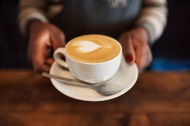 Bir Afrika barista ayakta kapuçino taze bir fincan kadar sunan bir kafe tezgahın arkasındaki closeup 