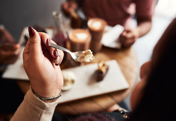 Young woman eating vanilla ice cream with a spoon while sitting at a cafe table with a friends in the background