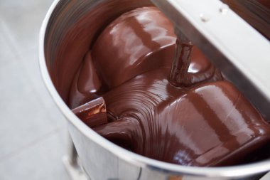 Closeup of melted chocolate being turned in a large stainless steel mixing machine in an artisanal chocolate making factory clipart