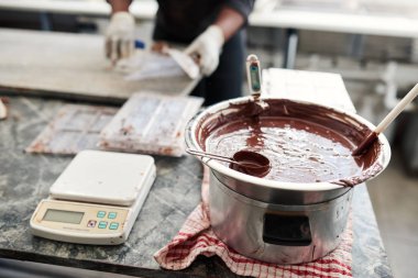 Melted chocolate in a bain marie on a table in an artisanal chocolate making factory being mixed and temperature monitored clipart