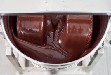Closeup of melted chocolate being turned in a large stainless steel mixer in an artisanal chocolate making factory clipart