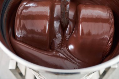 Closeup of melted chocolate turning in a large stainless steel mixer in an artisanal chocolate making factory clipart