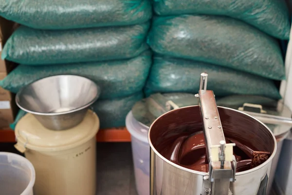 货架上的可可豆袋和在手工巧克力制造工厂的大型不锈钢搅拌机中融化的巧克力 — 图库照片
