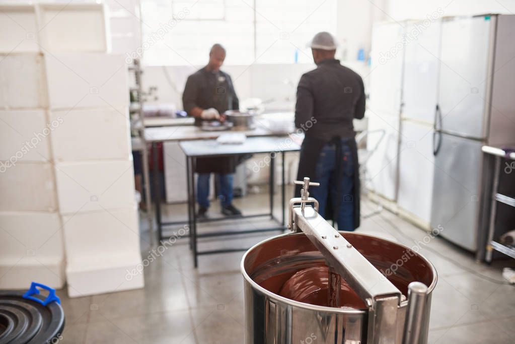 Two workers standing at a table in an artisanal chocolate making factory preparing chocolate to be melted and folded in a mixer