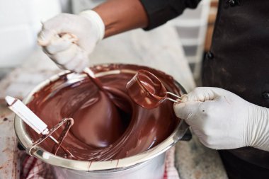 Closeup of a worker in an artisanal chocolate making factory mixing melted chocolate in bowl with a spoon clipart