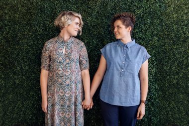 Genç lezbiyen çift birbirine birlikte yapraklı bir duvarın dışında önünde ellerini tutarak bakarak gülen