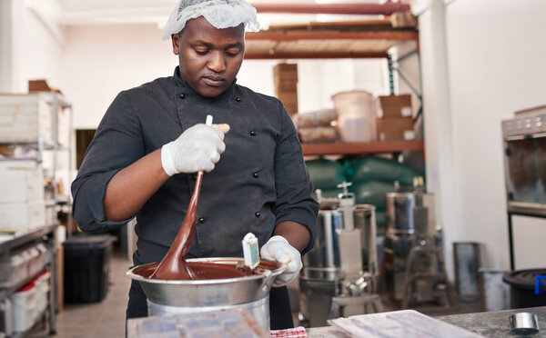 Worker standing at a table in an artisanal chocolate making factory mixing melted chocolate in a bain marie with a spoon