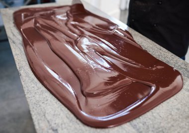Closeup of a worker spreading melting chocolate out on a table while working in an artisanal chocolate making factory clipart