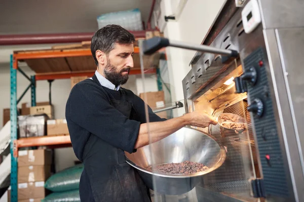 カカオ豆を焙煎機にボウルから配置する工場を作る職人のチョコレートのスモール ビジネス オーナー — ストック写真