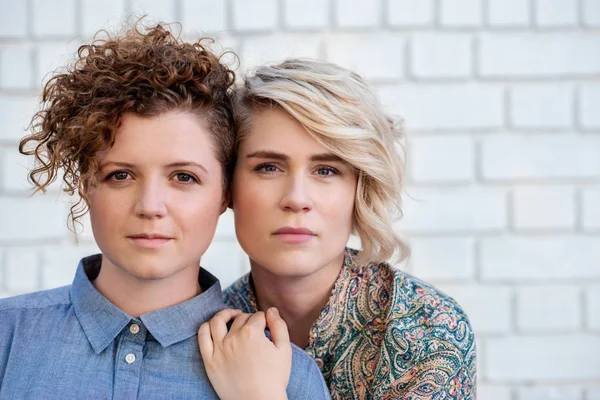 一对年轻的女同性恋夫妇一起站在外面的砖墙前的肖像 — 图库照片
