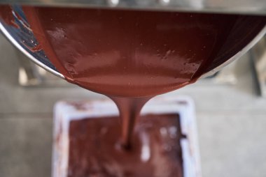 Closeup of melted chocolate pouring from a mixer into a container in an artisanal chocolate making factory  clipart