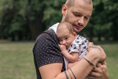 Bir sevgi dolu genç baba bebek oğlu onun omuz dışında duran bir parkta kucaklarken yakın çekim