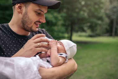 Erkek bebek onun kollarında tutarak ve onu bir parkta dışında dururken formül şişeyle besleme seven genç baba