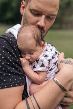 Onun bebek çocuk dışarıda duran bir parkta onun kollarında kucaklarken bakmakta genç baba