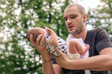 Bir içerik genç baba bebek oğlu dışında duran bir parkta elinde kucaklarken yakın çekim