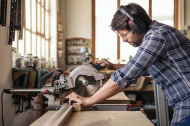 Bir parça tahta çalışırken yalnız ağaç işleme stüdyosunda kesmek için bir gönye kullanarak güvenlik dişli giymiş yetenekli woodworker gördüm