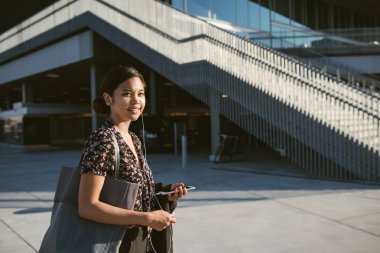 Dersten sonra okulda yürürken kulaklık müzik dinlerken gülümseyen Genç Asyalı üniversite öğrenci