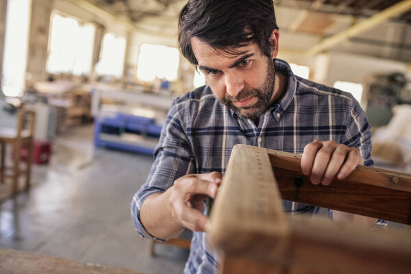Skilled furniture maker sanding a wooden chair on a bench while working alone in his woodworking shop