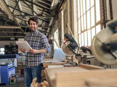 Bir tezgah marangozluk stüdyosunda gönüllülük tasarımları bir defter ile karşı yaslanmış bir gülümseyen woodworker portresi
