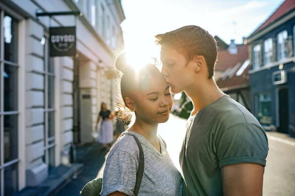 午後には街で一緒に立っている彼氏に額にキスされている若い女性の笑みを浮かべてください — ストック写真