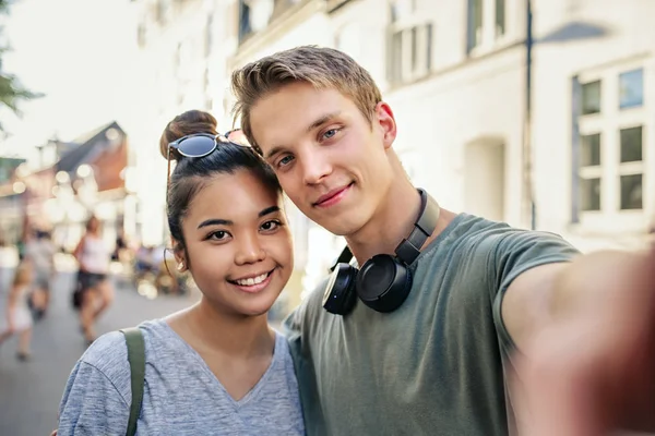 街の通りに立って腕ながら一緒に Selfie を取る若いカップルの笑顔 — ストック写真