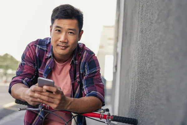 핸드폰에 텍스트를 보내는 보도에 자전거에 기대어 셔츠에 아시아 남자의 초상화 — 스톡 사진