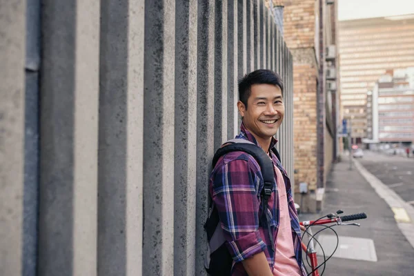 格子縞のシャツを自分の自転車と街の壁にもたれながら笑顔で若い男性の肖像画 — ストック写真