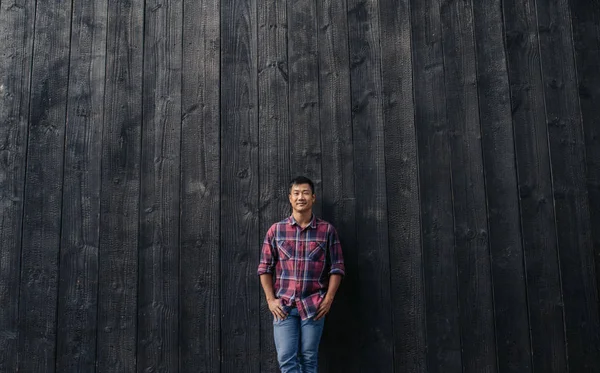 一个面带微笑的亚洲年轻人站在城市外的黑暗墙上 双手插在口袋里的肖像 — 图库照片