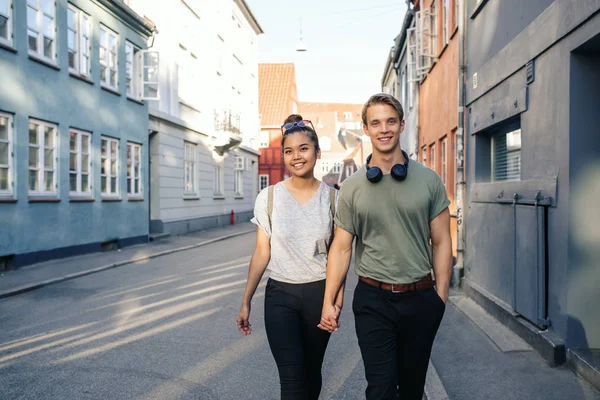 街の通りに沿って一緒に手をつないで歩きながら笑みを浮かべて愛情の若いカップル — ストック写真