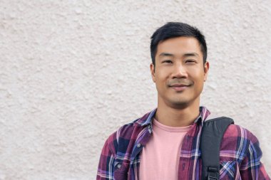 İçerik bir genç Asyalı adam bir sırt çantası taşıyan bir şehir sokakta bir duvar önünde ayakta portresi kapatın