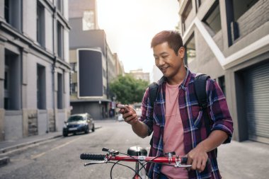 Genç Asyalı adam ile Onun Bisiklet şehir cadde boyunca yürürken bir cep telefonu üzerinde bir kısa mesaj okuma bir kareli gömlek gülümseyen