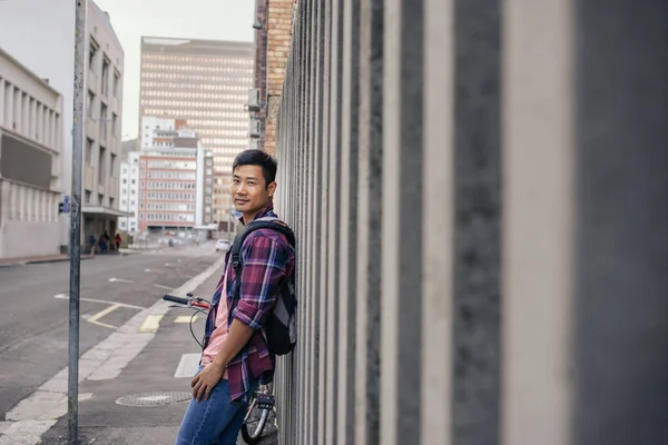 街の歩道の壁に乗って彼の自転車に傾いている格子柄のシャツの若いアジア人の肖像 — ストック写真