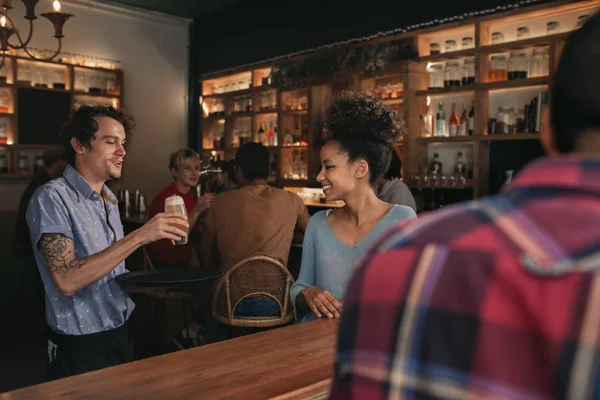 Smiling waiter bringing a drinks order to a group of smiling friends sitting together in a bar in the evening