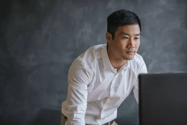 Konzentrierter Asiatischer Geschäftsmann Lehnt Sich Über Seinen Schreibtisch Vor Einer — Stockfoto