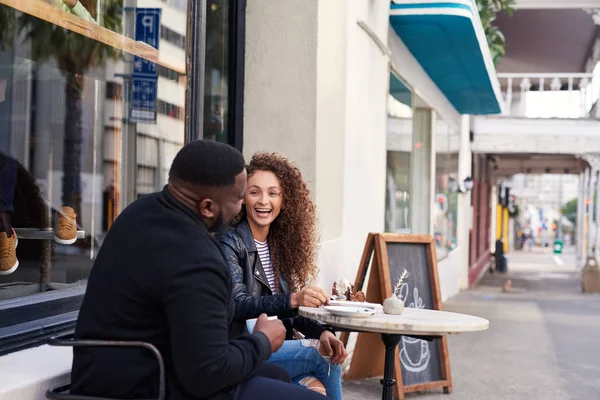 两个面带微笑的年轻朋友一边谈笑风生 一边坐在人行道上的咖啡馆里喝酒 吃蛋糕的桌子旁 — 图库照片