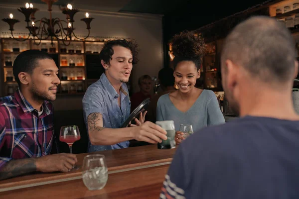 Waiter bringing a drinks order to a group of smiling friends enjoying a night out together in a bar