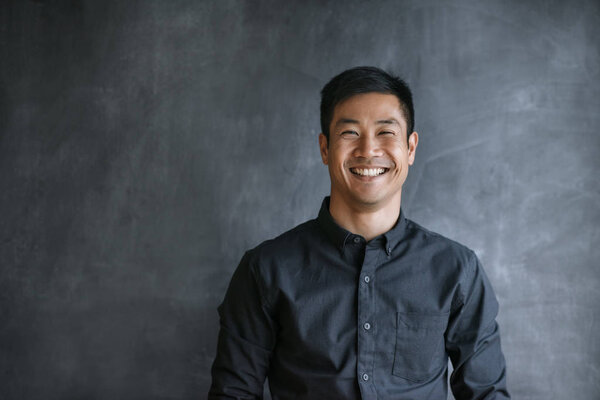 Портрет молодого азиатского бизнесмена, стоящего у стола в офисе
