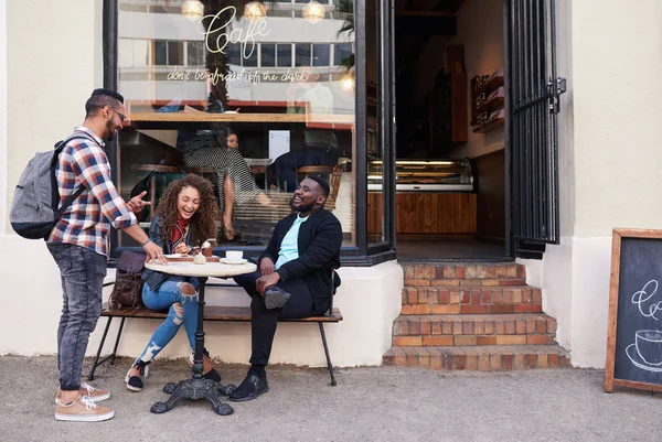 两个面带微笑的年轻人和朋友一边谈笑风生 一边坐在人行道上的咖啡馆里喝酒 吃蛋糕的桌子旁 — 图库照片