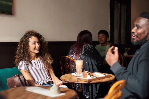 两个年轻的朋友一边喝咖啡一边笑 一边在一家时髦的咖啡馆里聊天 — 图库照片