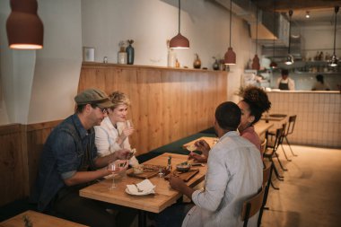 Gözde bir barda bir masada bir arada oturup yemek paylaşan gülümseyen genç arkadaşlar çeşitli grup 