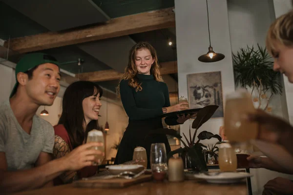 微笑的女服务员带着饮料订单给一群年轻的朋友 一起在酒吧里过夜 — 图库照片