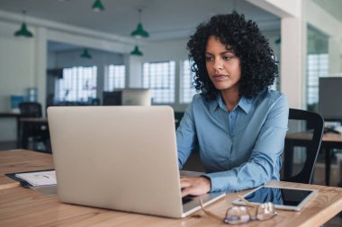 Kendini adamış olgun iş kadını bir dizüstü bilgisayar ile online çalışan büyük bir modern ofiste masasında oturan