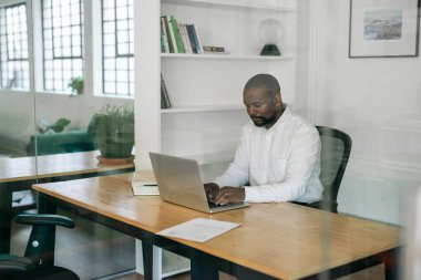 Afro-Amerikan yöneticisi modern ofisinde masasında otururken bir dizüstü bilgisayar ile online çalışma