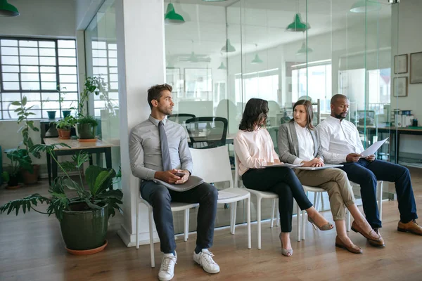 Diverse group of job applicants sitting together outside of an office waiting for their interviews